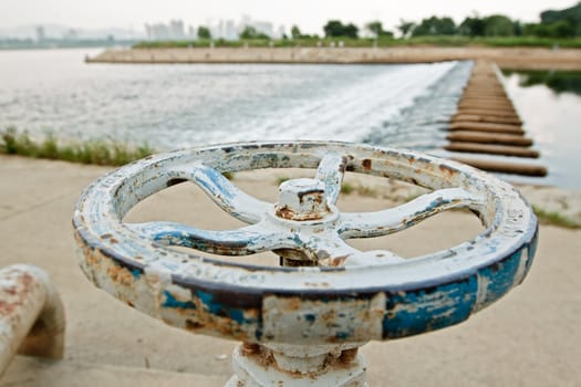 White and blue rusty industrial faucet wheel with shallow dof on river background