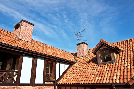 Red tile roof with chimneys and antennas on blue sky background