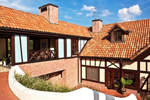 A house with red tile roof with chimneys and antennas on blue sky background