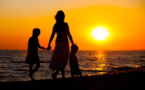 Mother and her kids silhouettes on beach at sunset