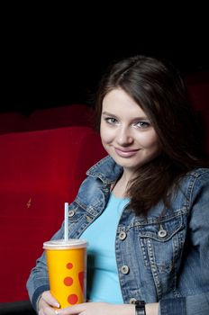 beautiful woman in a movie theater, watching a movie and drink a drink