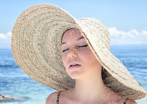 Young, beautiful  woman wearing a straw hat on the beach