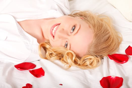 happy blonde woman in bed with red rose petals