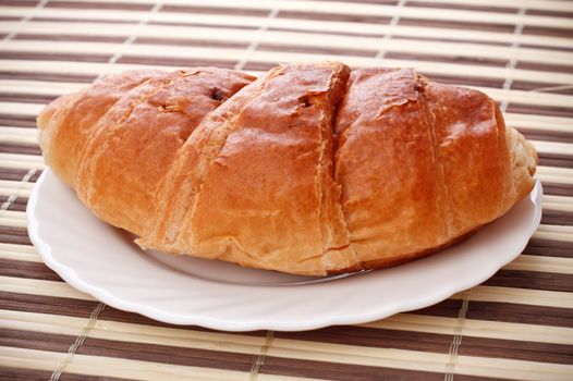 single fresh croissant laying on white dish