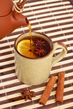 pouring tea in mug with cinnamon and star anise on bamboo napkin