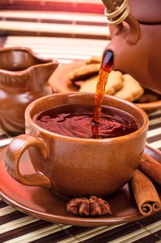 pouring tea in cup with cinnamon and star anise on bamboo napkin