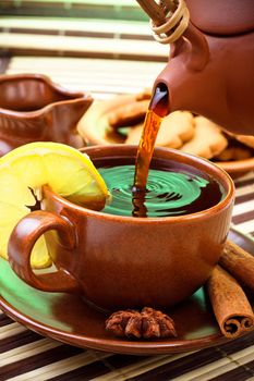 pouring tea in cup with cinnamon and star anise on bamboo napkin
