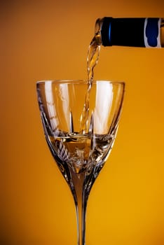 white wine pouring in glass, yellow background