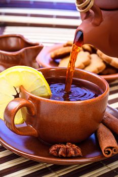 pouring tea in cup with cinnamon and star anise on bamboo napkin