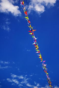 Multi colored party flags on a line on a background of blue sky with fluffy white clouds 