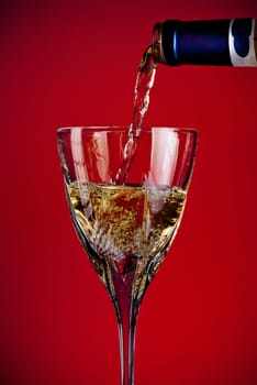 white wine pouring in glass, red background