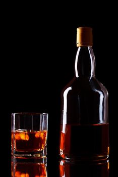 bottle and glass of whiskey on black background