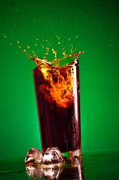 glass with splashing cola on green background