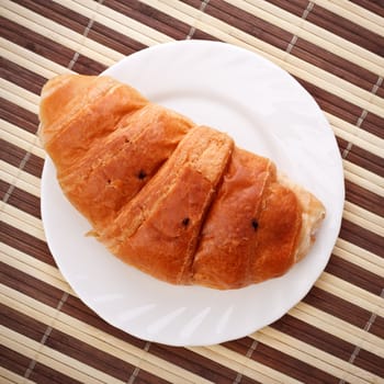 single fresh croissant laying on white dish