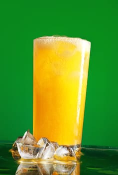 glass of orange soda with ice over green background