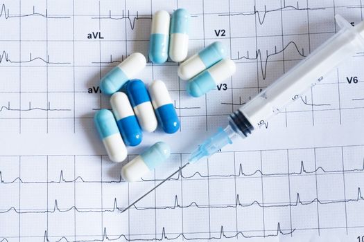 Syringe and tablets on the paper with graph of heart rhythm
