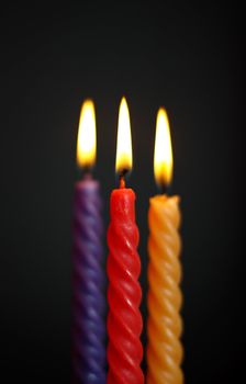 three twisted burning candles over black background