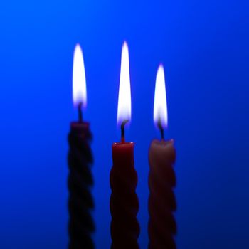 three twisted burning candles over blue background