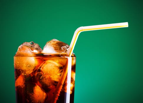 glass of cola with ice and straw on green background