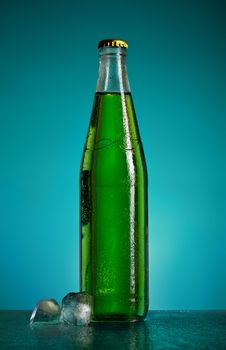 green soda bottle and ice cubes, blue background