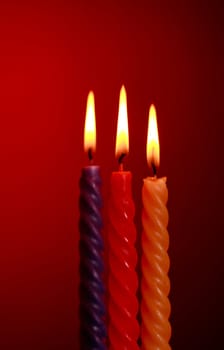 three twisted burning candles over red background