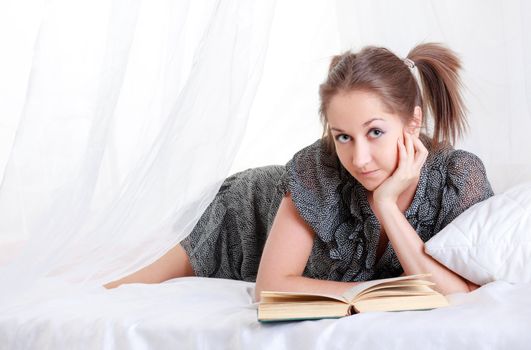 girl with pigtails reading book laying in bed