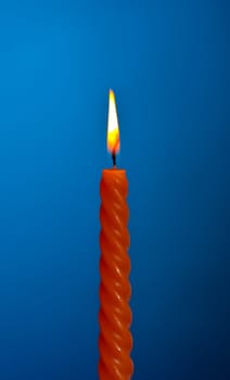 single twisted burning candle over blue background