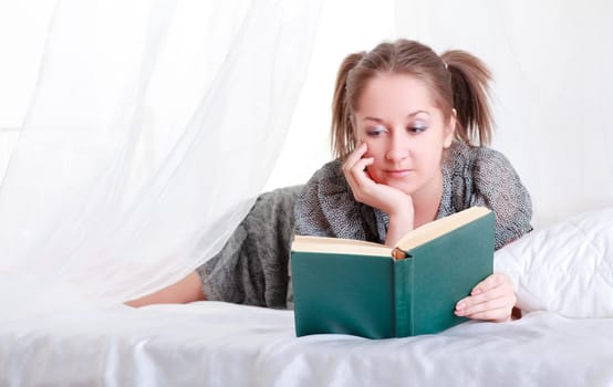 girl with pigtails reading book laying in bed