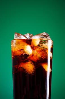 glass of cola with ice on green background