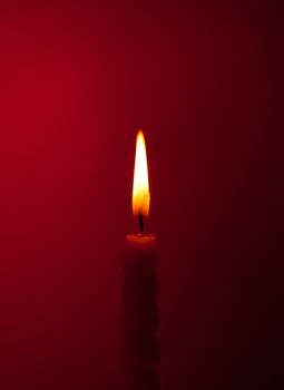 one twisted burning candle over red background