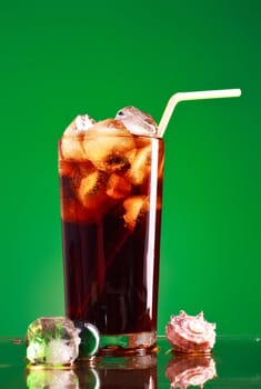 glass of cola with ice and straw on green background