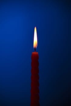 single twisted burning candle over blue background