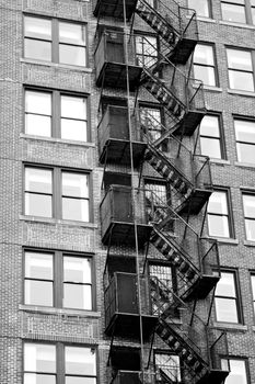 Exterior fire escape stairs on the outside of an old brick building in black and white.