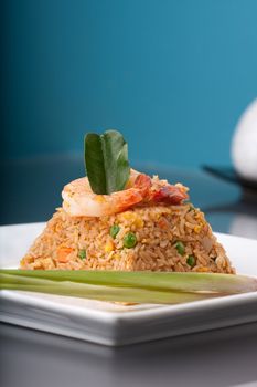 Thai style shrimp fried rice presented on a square white plate in the shape of a pyramid.