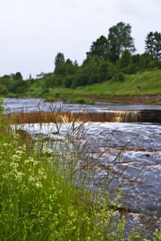 green grass and rough river with small waterfall