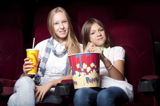 two girls look three-dimensional cinema, sitting in the glasses, eat popcorn, drink drink