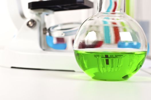 lab bottle with green liquid, in the background microscope and other items