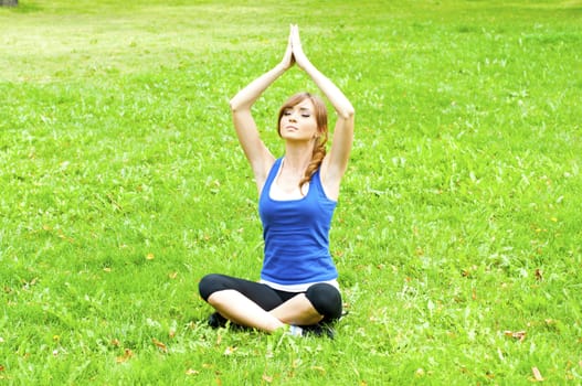 young woman is engaged in yoga, in summer forest on a green grass