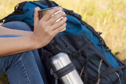 woman, resting, drinking a drink next to a backpack and is worth a thermos