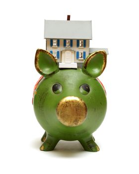 A miniature house rests on a piggy bank for monetary concepts.