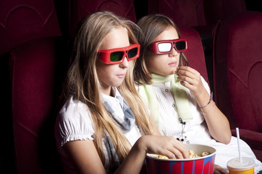 two girls look three-dimensional cinema, sitting in the glasses, eat popcorn, drink drink