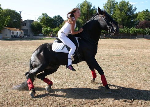 young woman and his black stallion in  a field