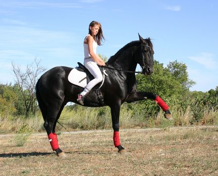 young woman and his black stallion in  a field