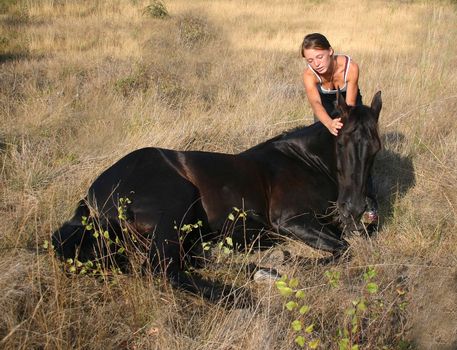 young riding girl and her black stallion laid down