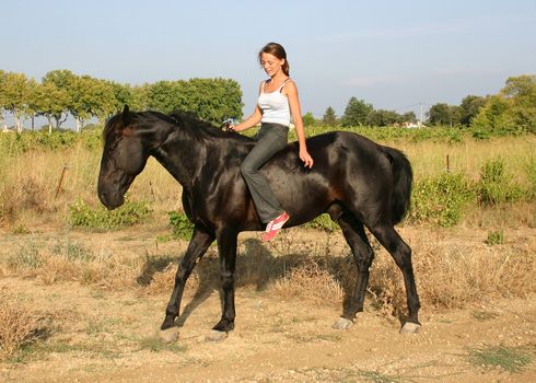 young woman and his black stallion in  a field