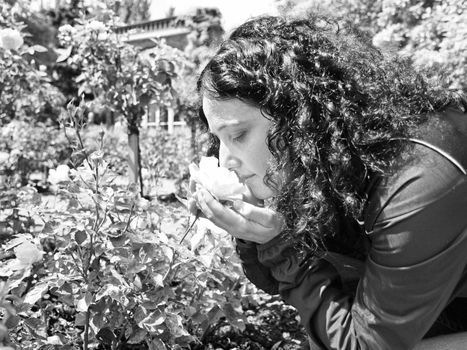 Pretty young brunette girl woman female smelling roses in a park