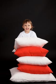 boy with pile of cushions on black background