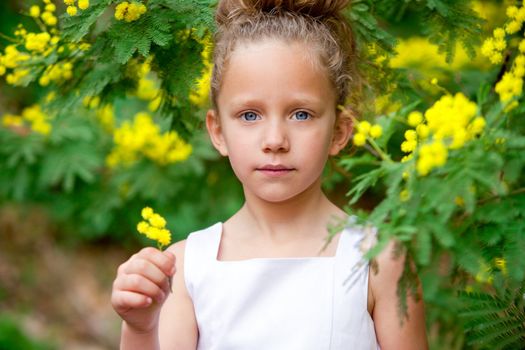 Close up portrait of cute little girl holding yellow flowers outdoors.