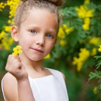Close up portrait  of cute little girl showing yellow flower outdoors.