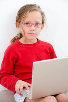 Portrait of cute blond girl doing homework with laptop.